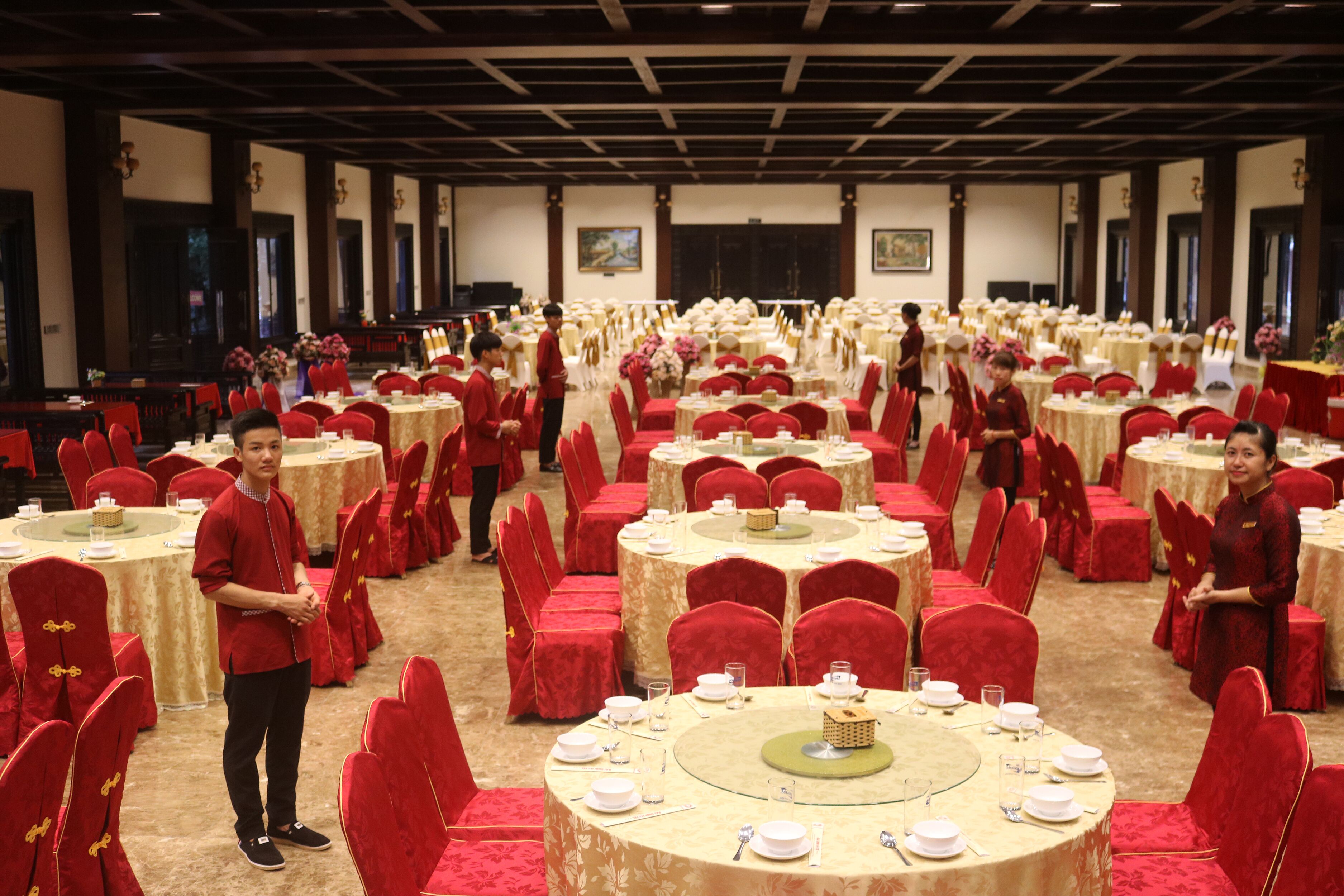 Un salón de banquetes con mesas redondas dispuestas para comer, sillas rojas y personal uniformado.
