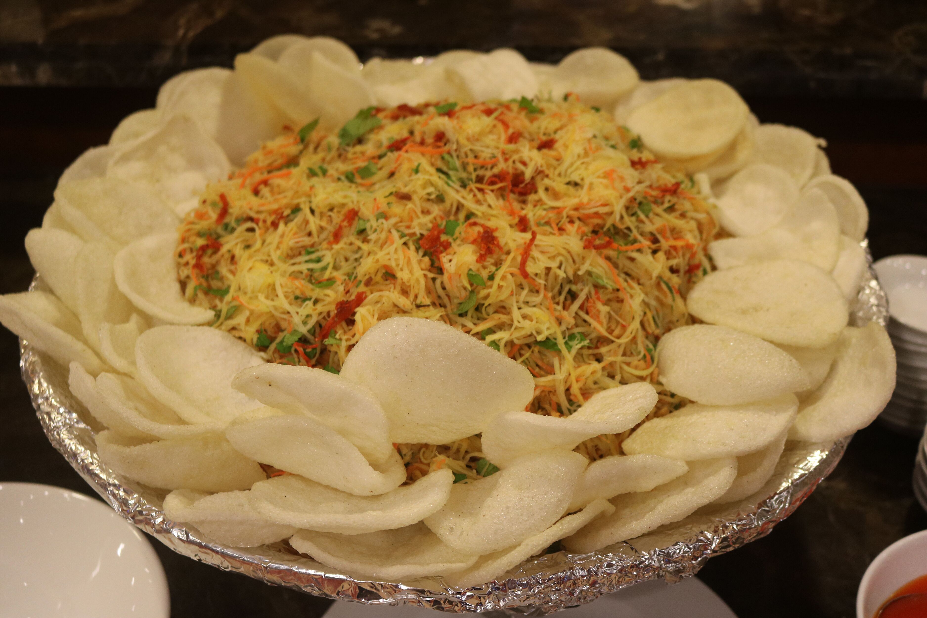 A dish with shredded vegetables and potato slices in a foil container.