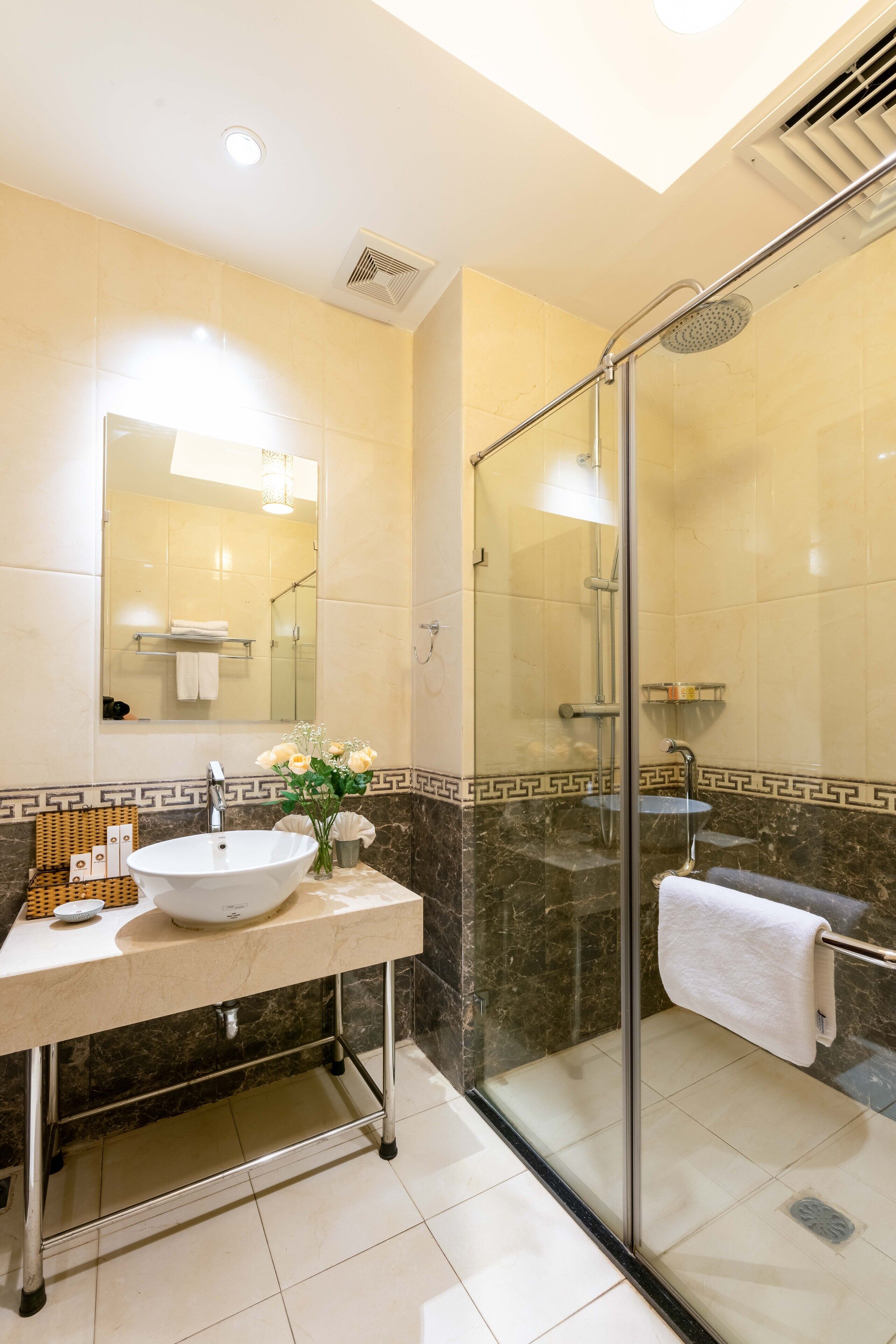 A modern bathroom with a glass-enclosed shower, a sink with a vase of flowers, and a mirror above the sink.