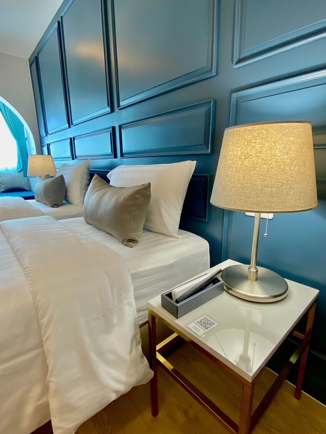 A hotel room with a large bed, a bedside table with a lamp, and a window with curtains.