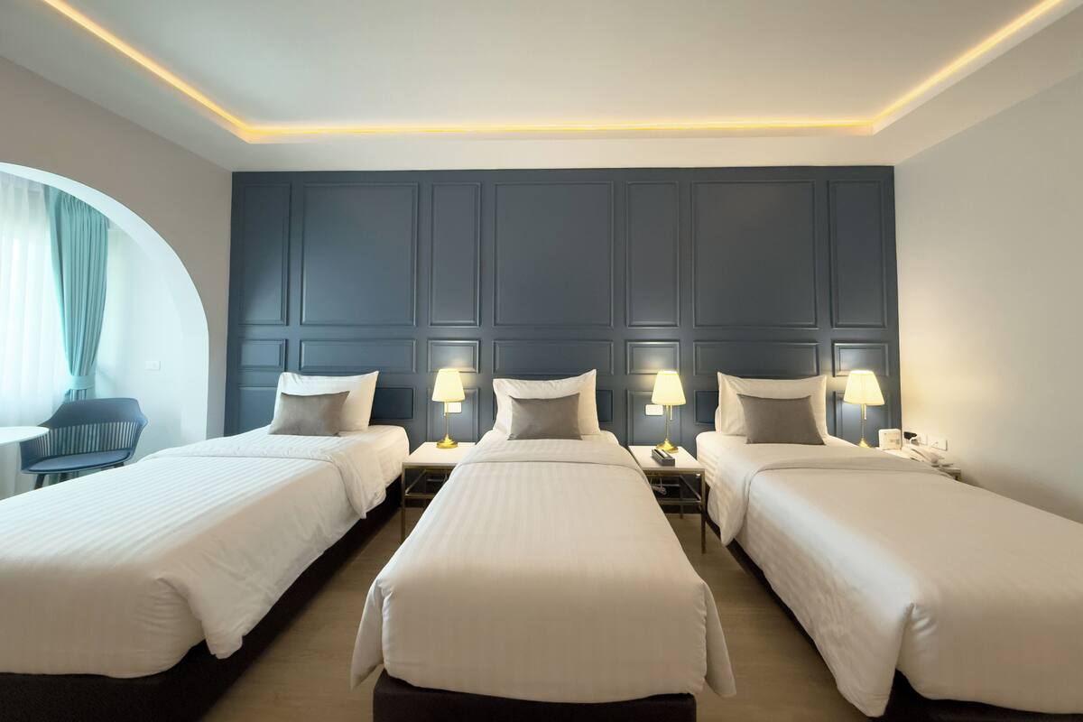 A hotel room with three single beds, a desk, and two bedside tables with lamps.