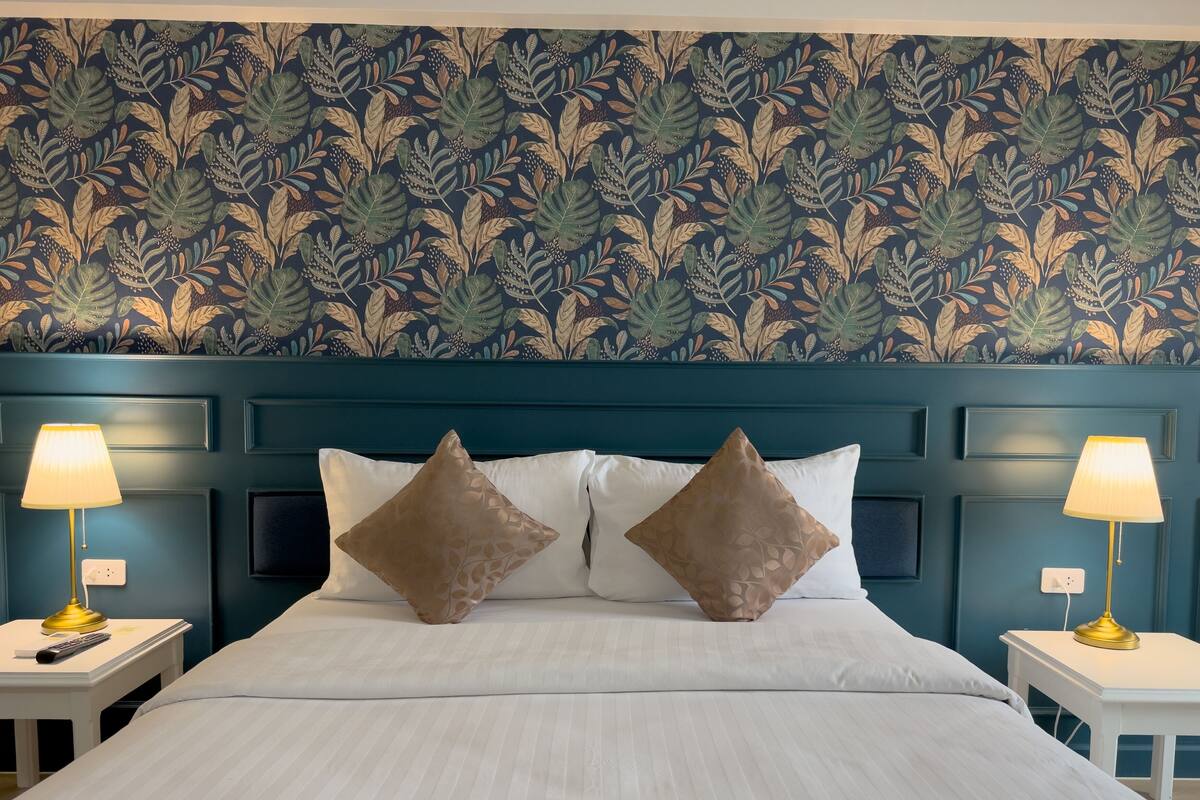 A hotel room with a large bed, two bedside tables with lamps, and a decorative leaf-patterned wallpaper.