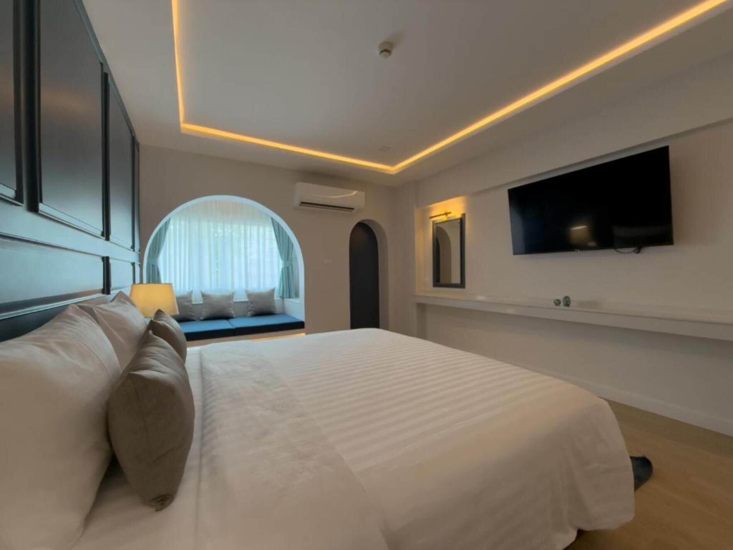 A modern bedroom with a large bed, a TV mounted on the wall, and a window with a view.