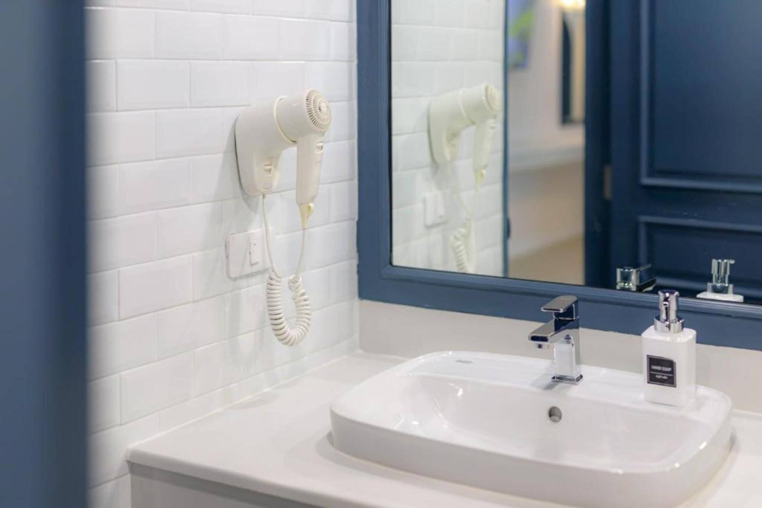 A bathroom with a white sink, a mirror, and a hairdryer mounted on the wall.