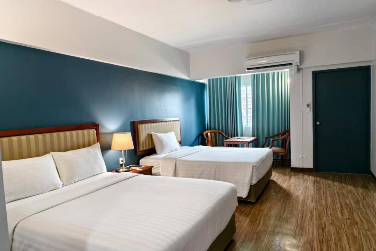 A hotel room with two beds, a desk, a chair, and an air conditioning unit.