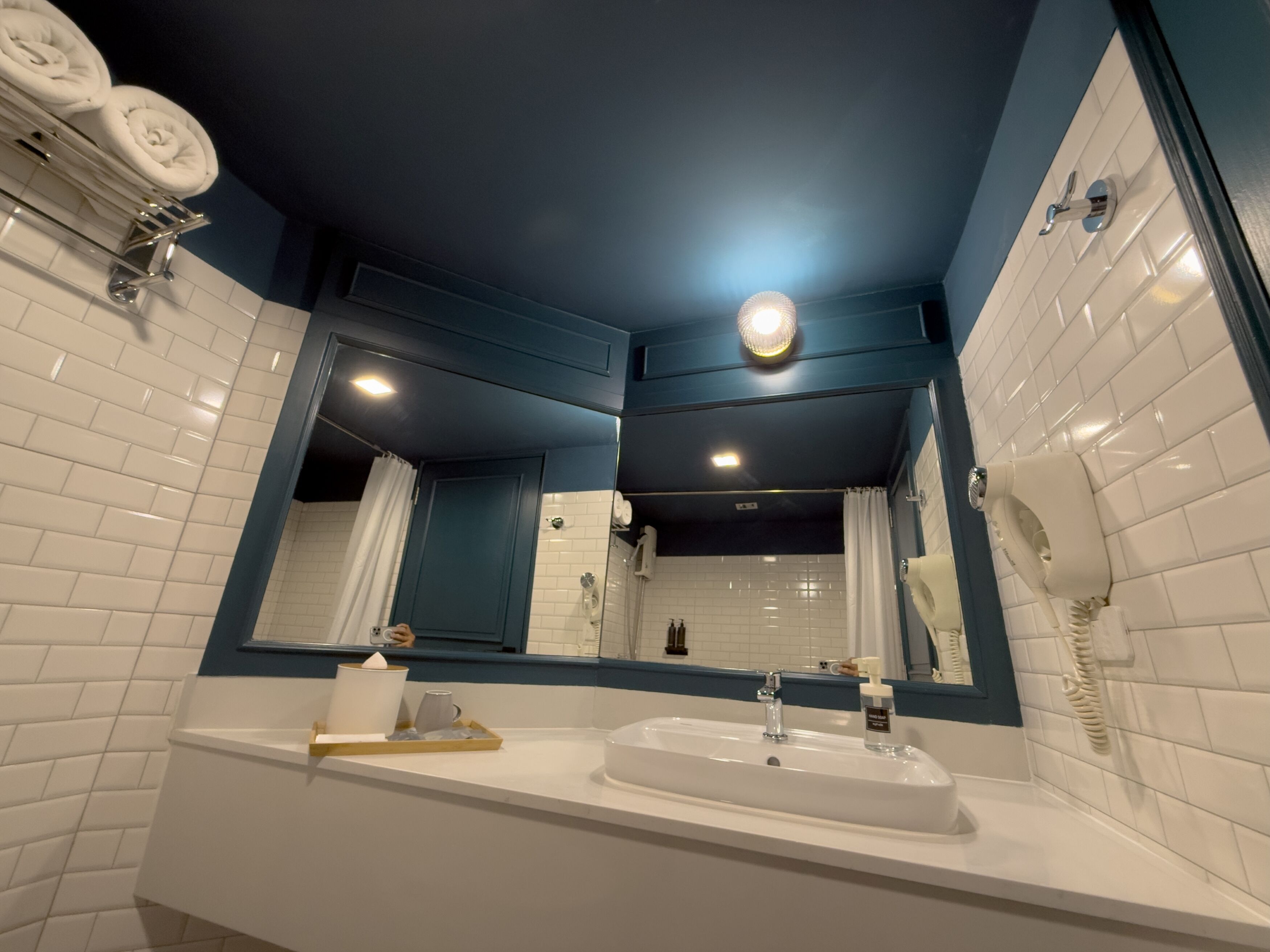 Un baño moderno con un lavabo blanco, un espejo, un perchero para toallas y una zona de ducha.