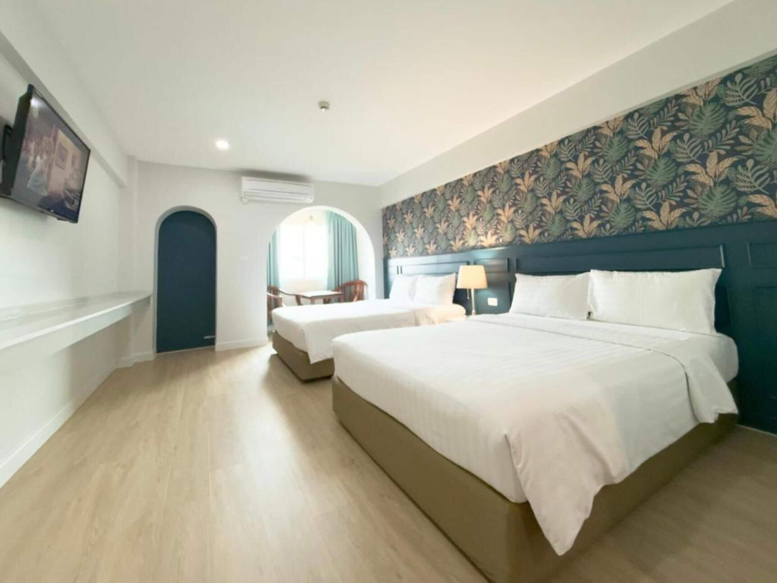 Une chambre d’hôtel avec un grand lit, un lit plus petit, un bureau avec une chaise, une lampe et un téléviseur fixé au mur.