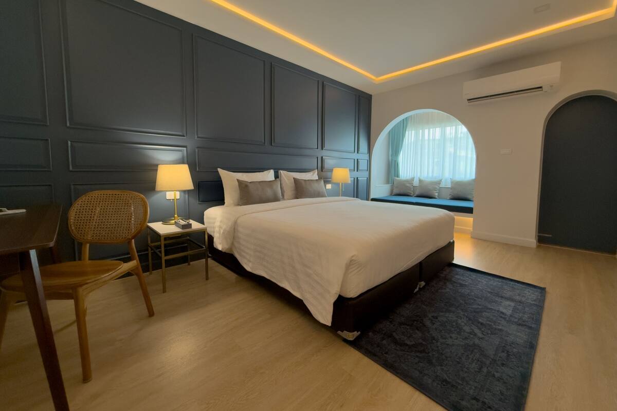 A modern bedroom with a large bed, bedside tables, a desk, and a window with a view.