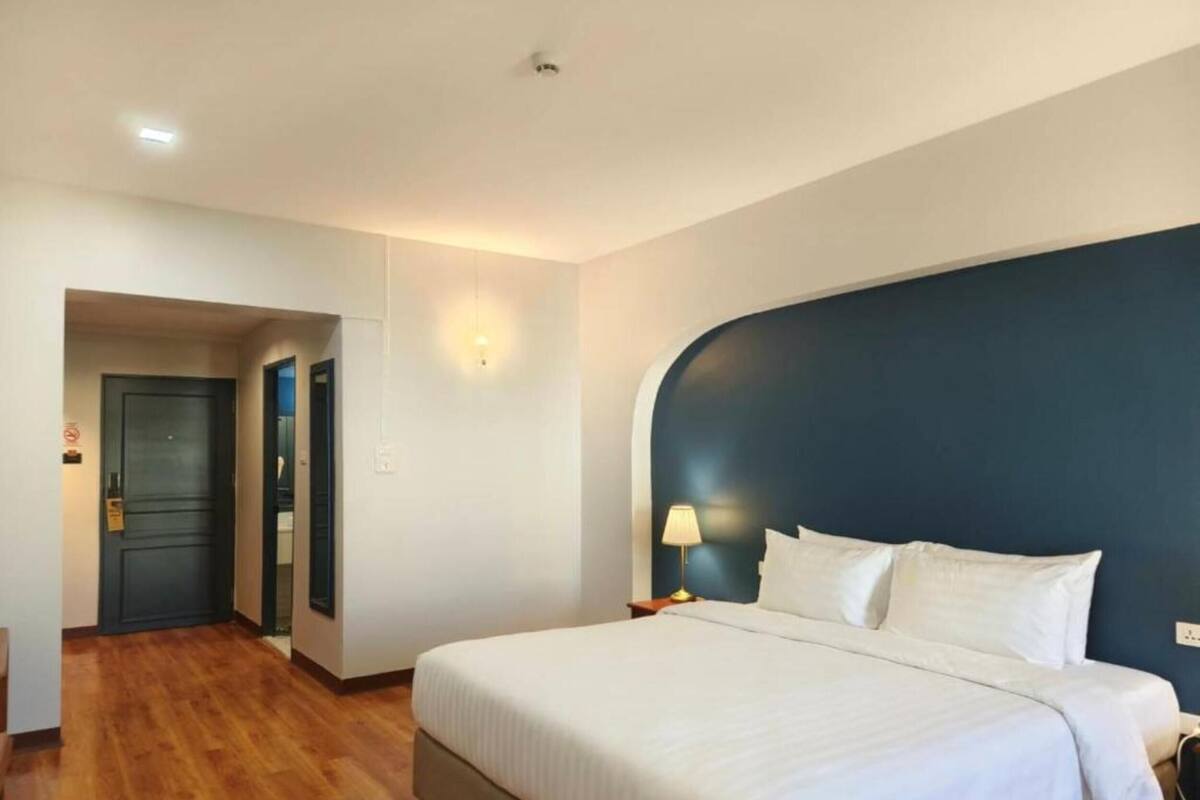 A hotel room with a large bed, a nightstand, a lamp, and a door leading to another room.