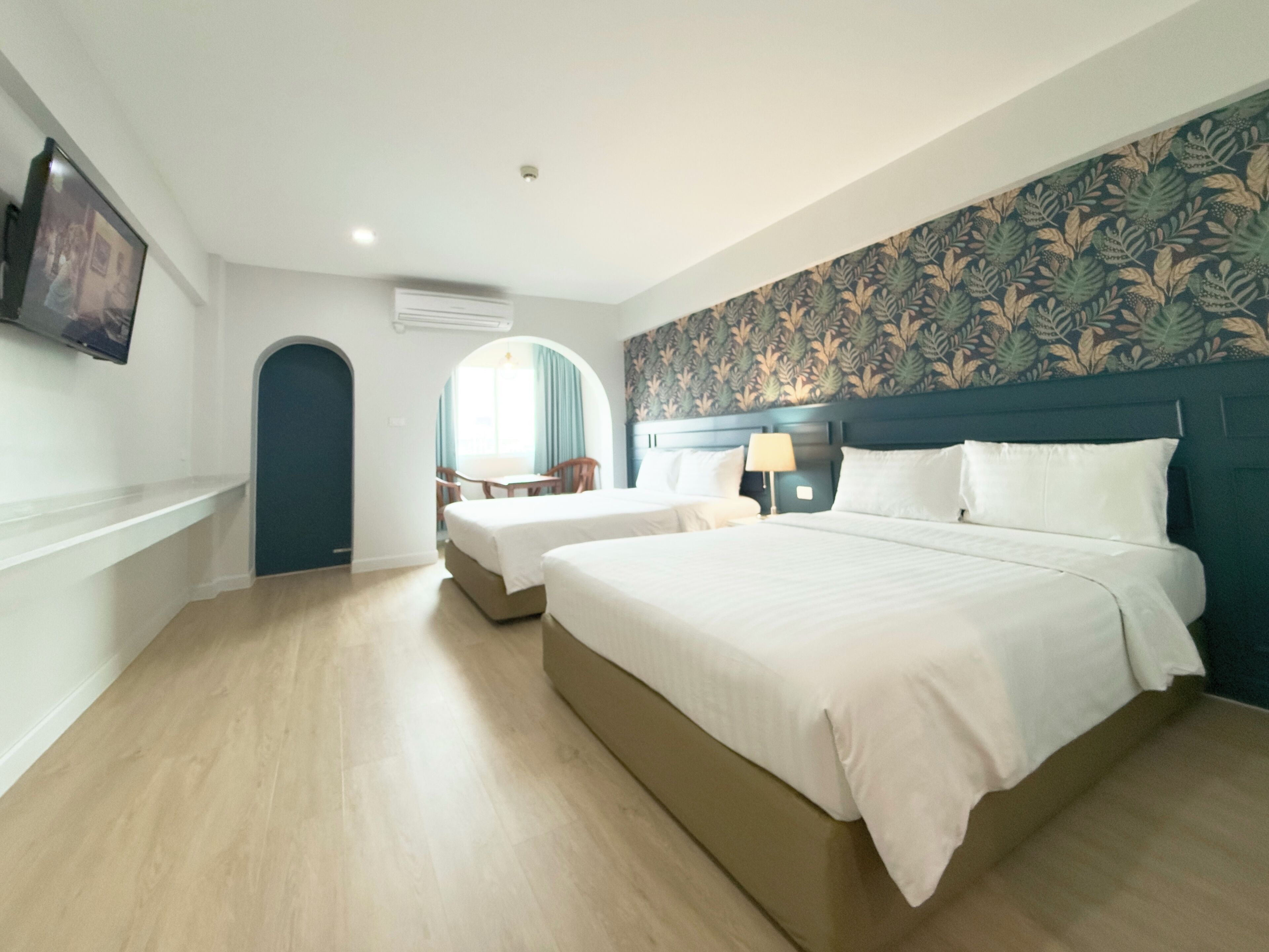 Una habitación de hotel con una cama grande, una cama más pequeña, un escritorio con silla y una ventana con cortinas.