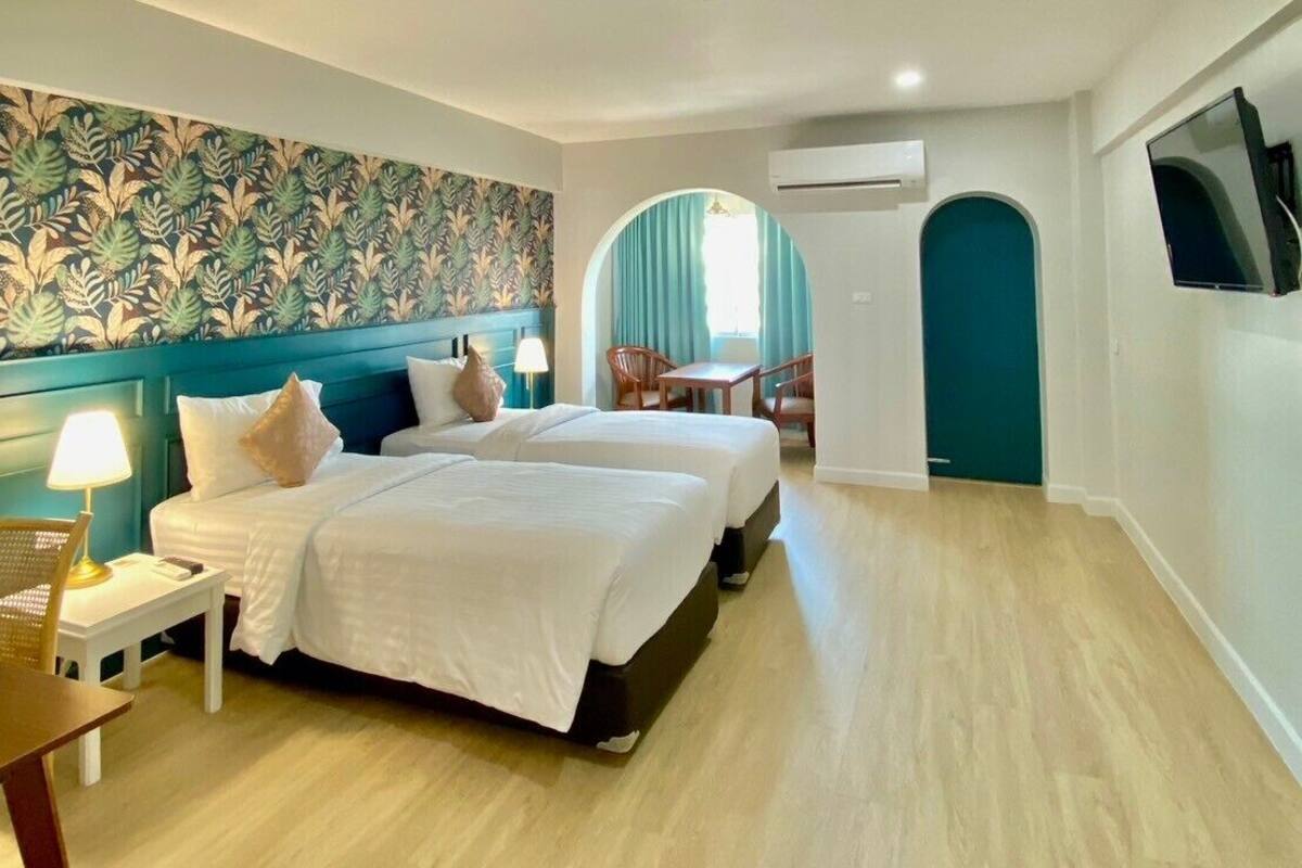 A hotel room with two beds, a desk, a chair, a TV, and an arched doorway.