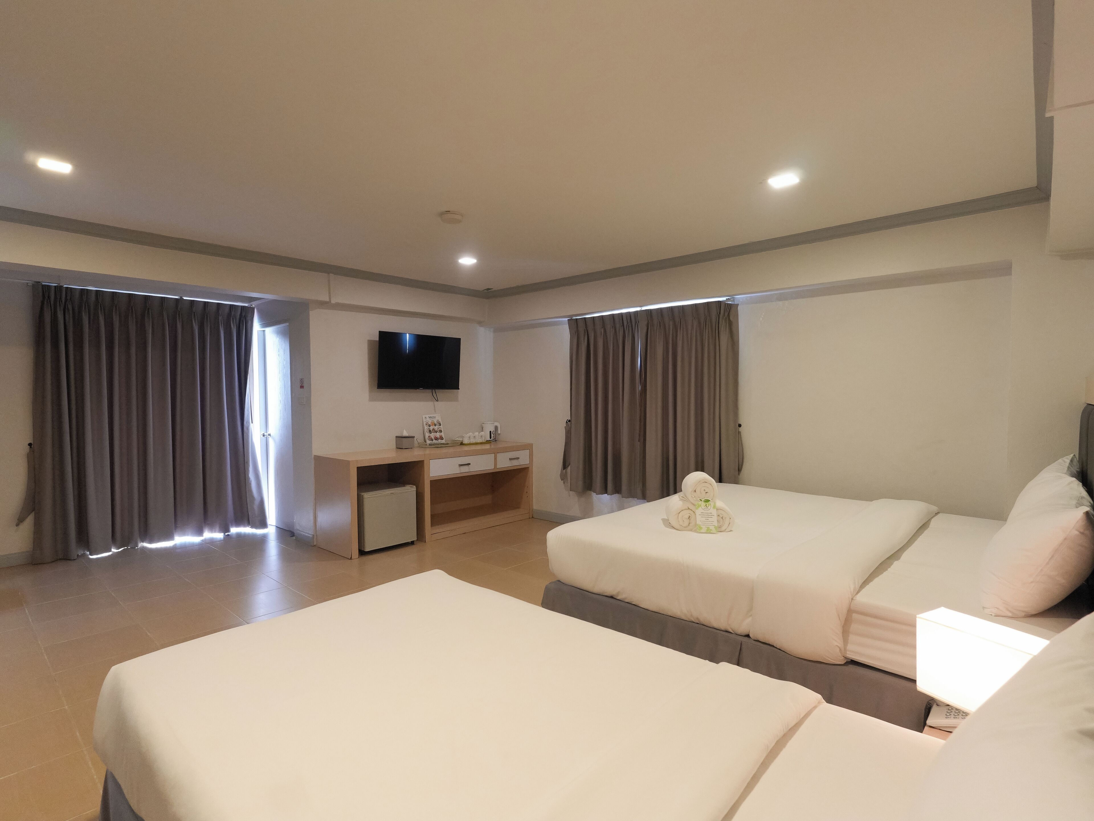 A hotel room with two beds, a desk, a TV, and a small refrigerator.