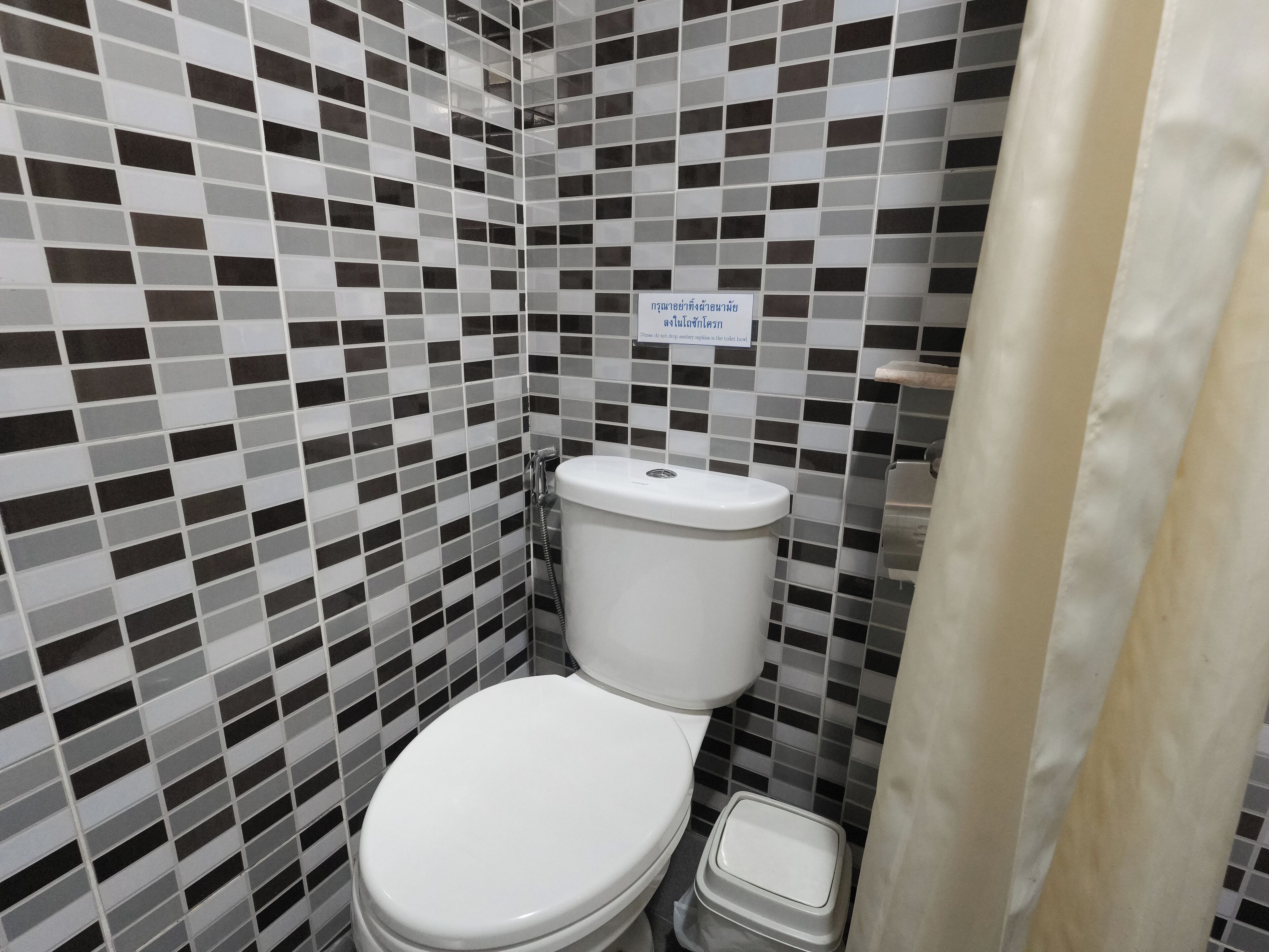 A bathroom with a tiled wall, a toilet, and a shower curtain.