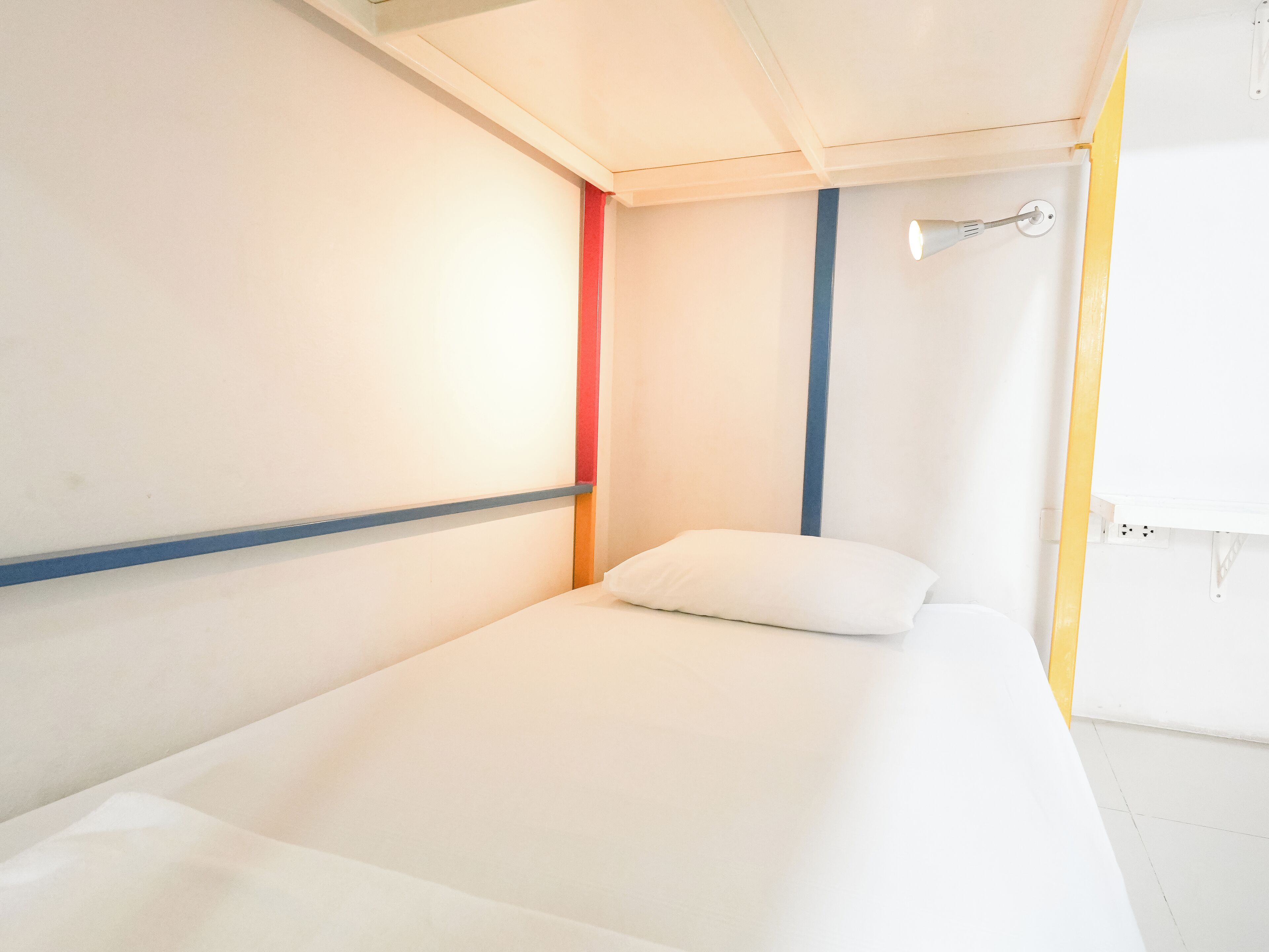 A single-bed room with a white bed, a red wall, and a blue accent wall.