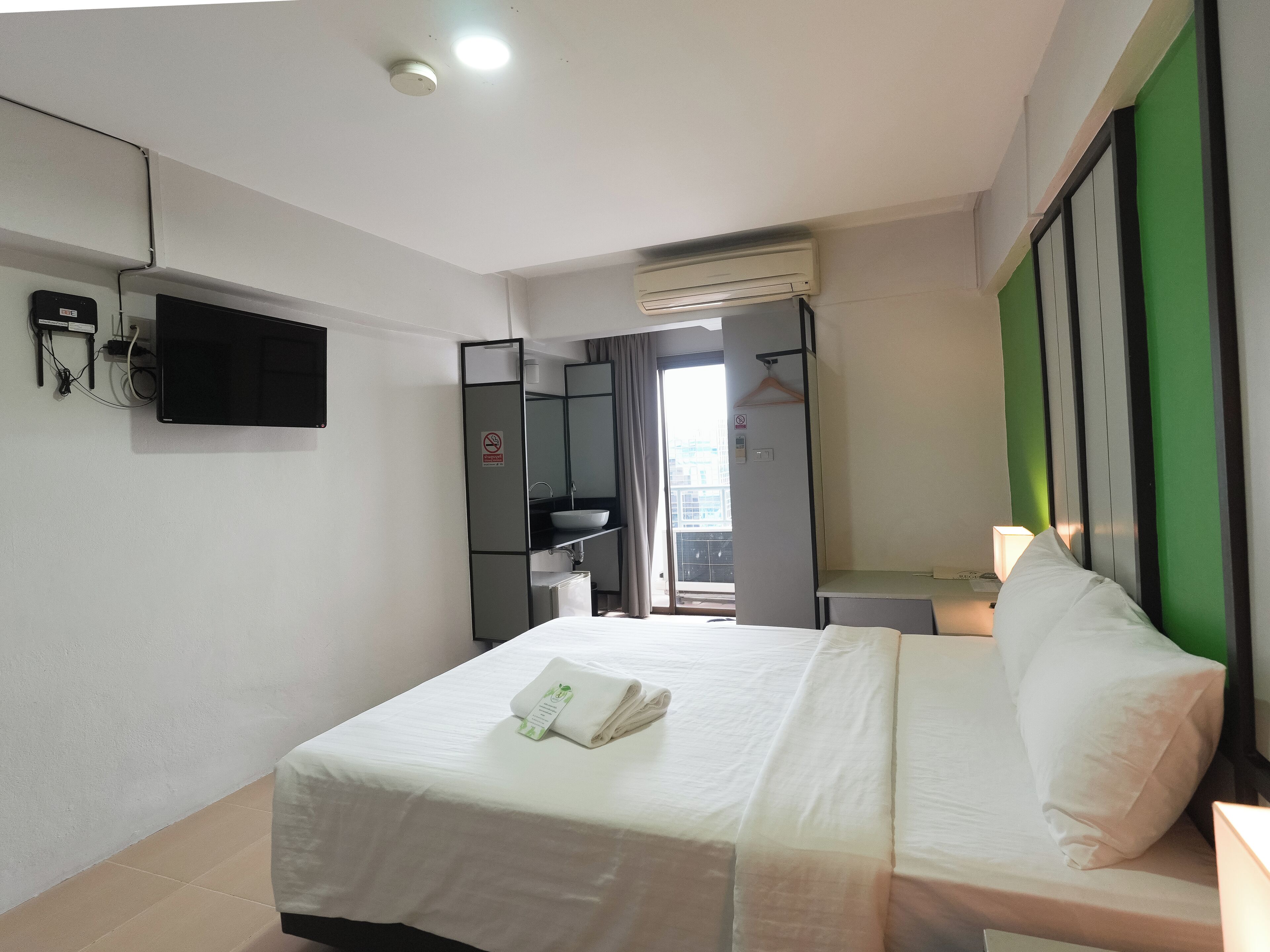 Una habitación de hotel con cama, televisión, armario, lavabo y ventana.