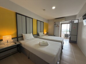 A hotel room with two beds, a desk, a lamp, and a view of the outside. - Regent Ngamwongwan (Nonthaburi)
