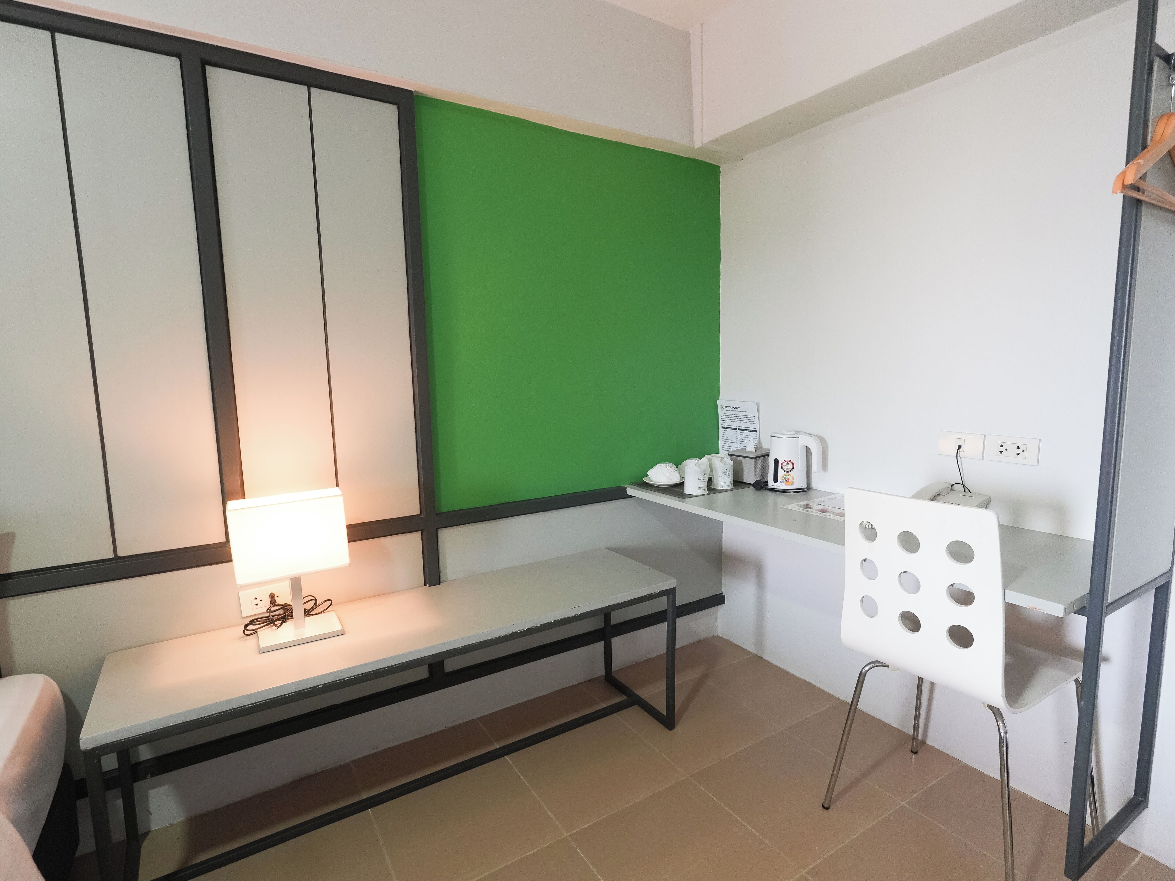 A small, modern room with a white desk, a green screen, and a white chair with circular cutouts.