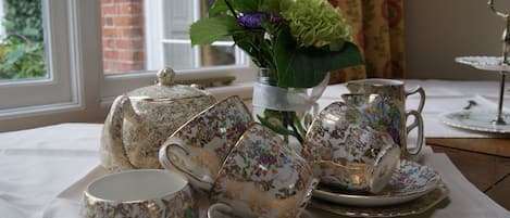 Une table dressée avec un service à thé comprenant des théières, des tasses et des soucoupes, et un vase de fleurs en arrière-plan.