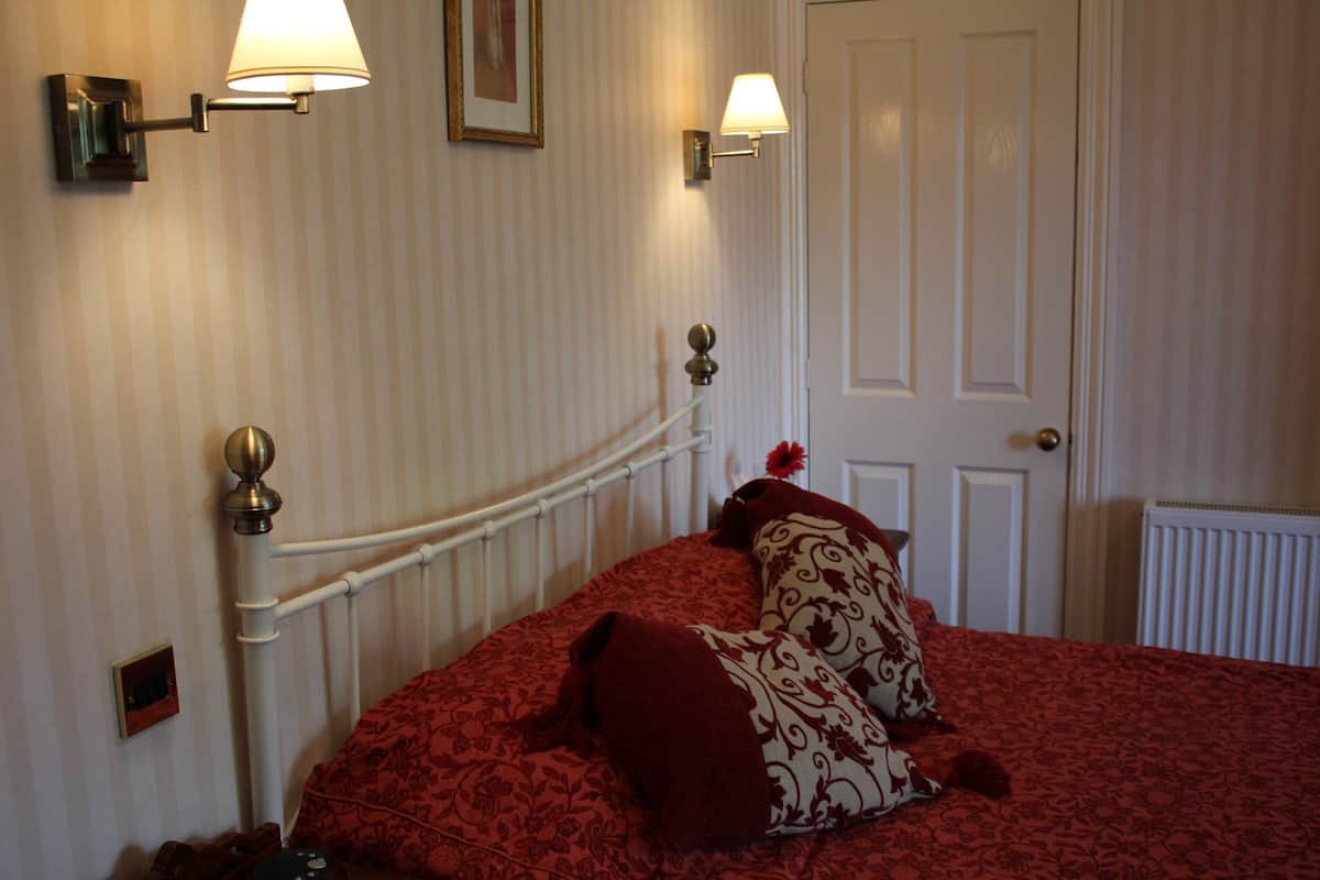 A hotel room with a bed, two wall-mounted lamps, a door, and a radiator.