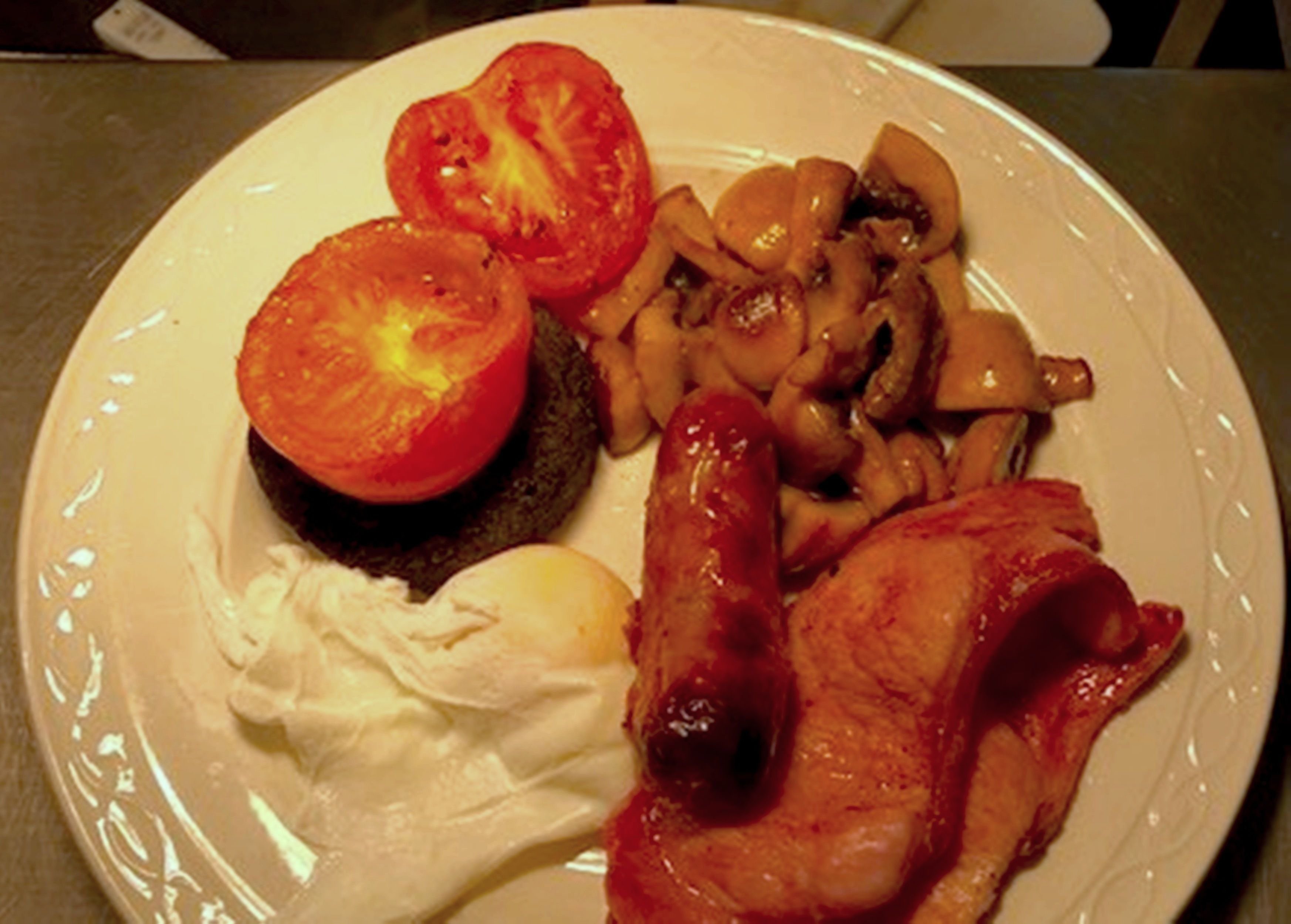 Een bord met een plak tomaat, champignons, een stukje vlees en een lepel slagroom.