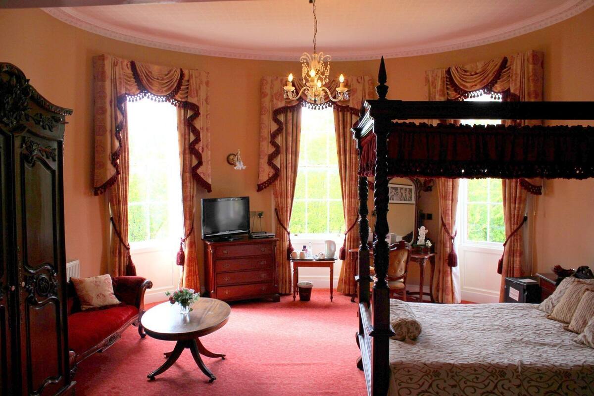 A bedroom with a four-poster bed, a television, a desk, and a chair.