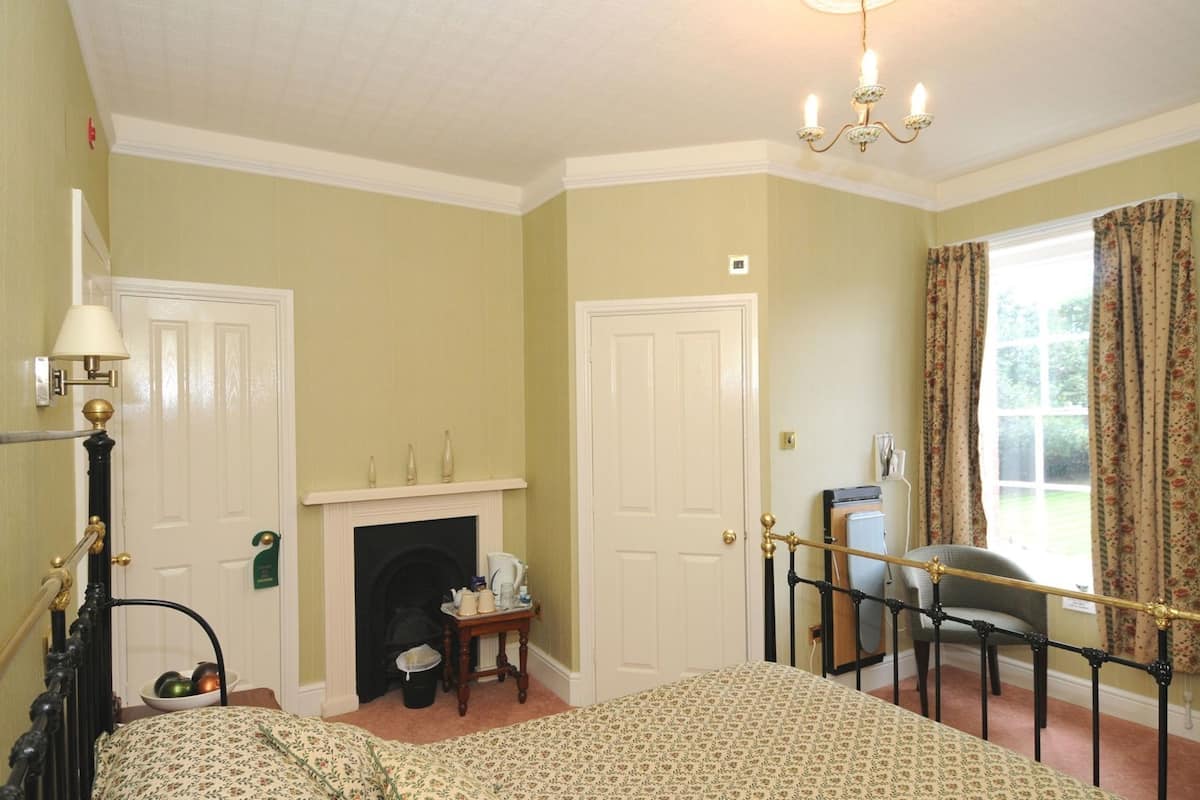 A bedroom with a bed, a fireplace, a chair, a desk, and a window with curtains.