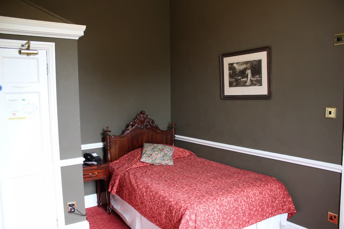 A bedroom with a wooden bed, a bedside table with a telephone, and a framed picture on the wall.