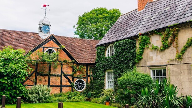 A traditional Tudor-style building with a thatched roof, a visible chimney, and a weather vane.