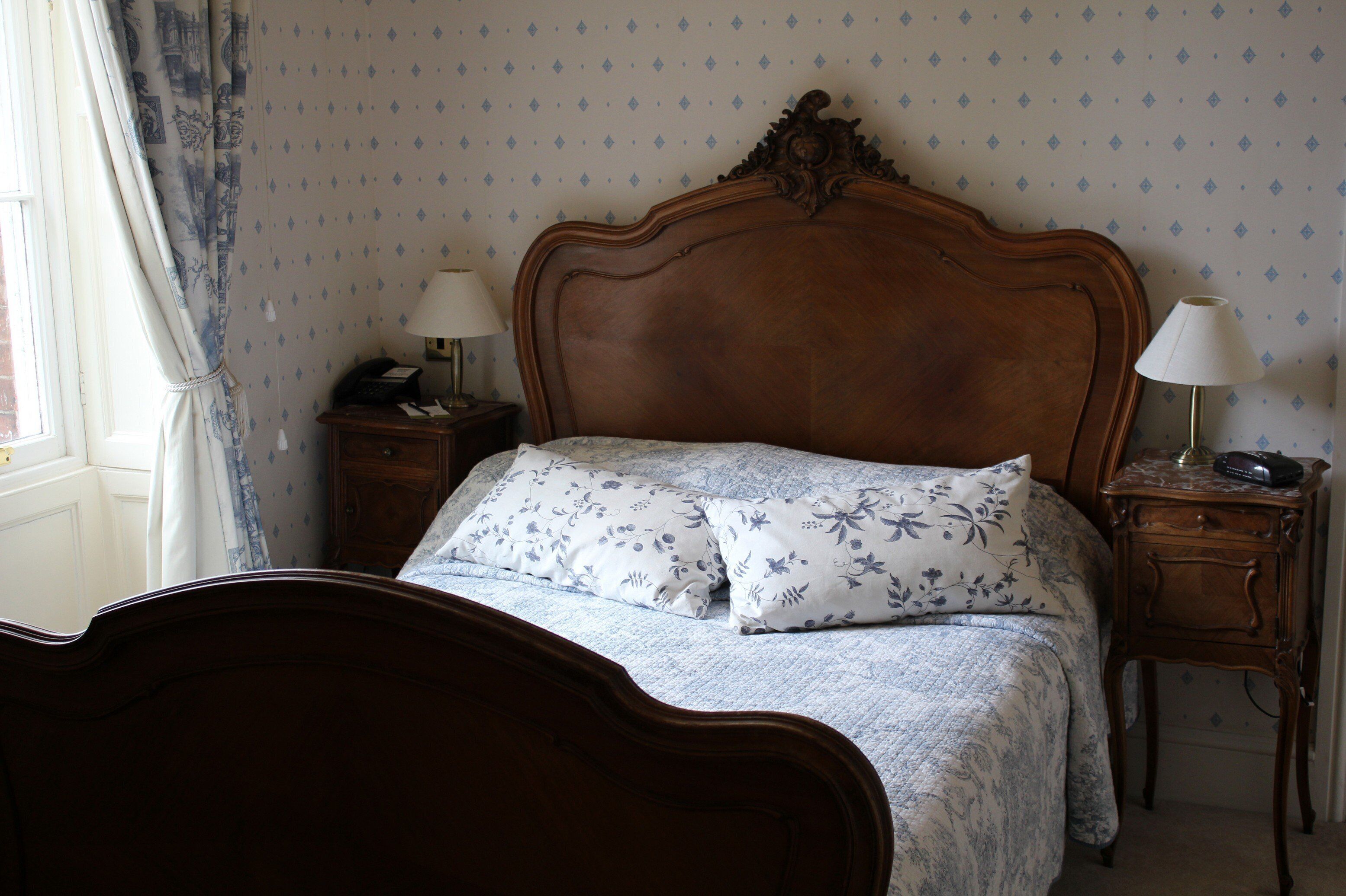 A neatly made bed with floral bedding, two bedside tables with lamps, and a patterned wallpaper.
