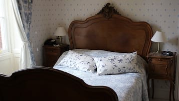 A neatly made bed with floral bedding, two bedside tables with lamps, and a patterned wallpaper.