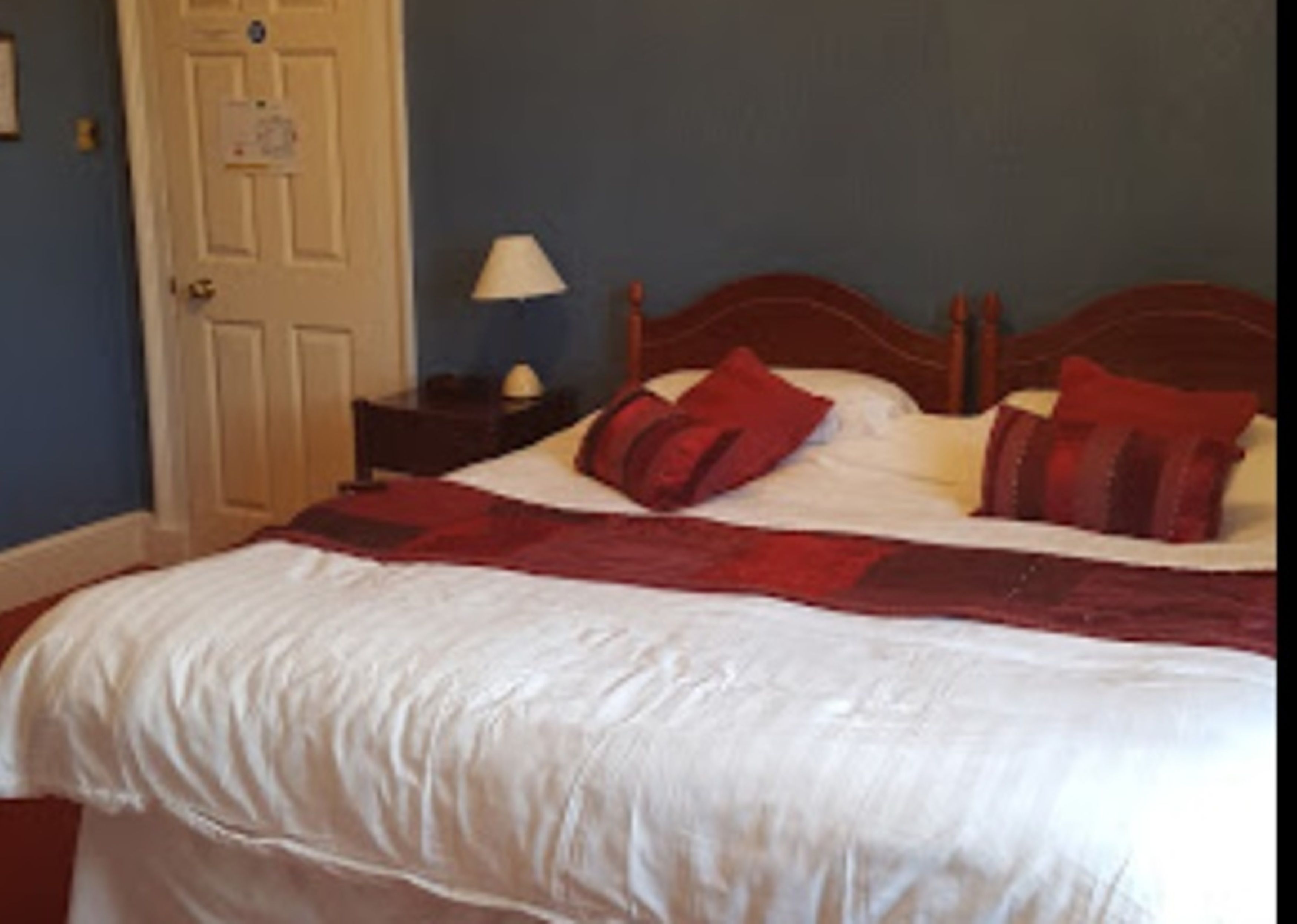 A bedroom with a bed, a nightstand, a lamp, and a door.