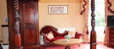 A room with a four-poster bed, a red velvet sofa, a wooden cabinet, and a television.