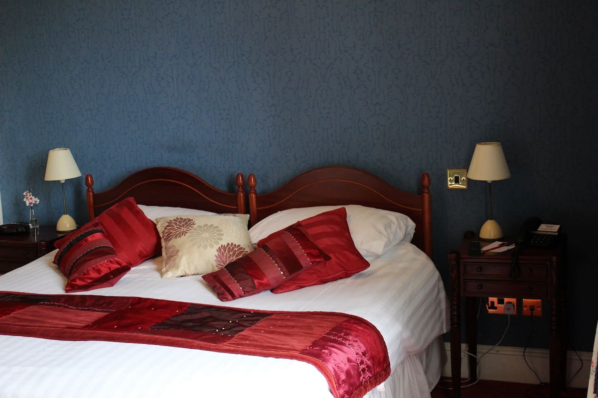 A neatly made bed with a red and white bedspread, two bedside lamps, and a nightstand with a lamp and a phone.