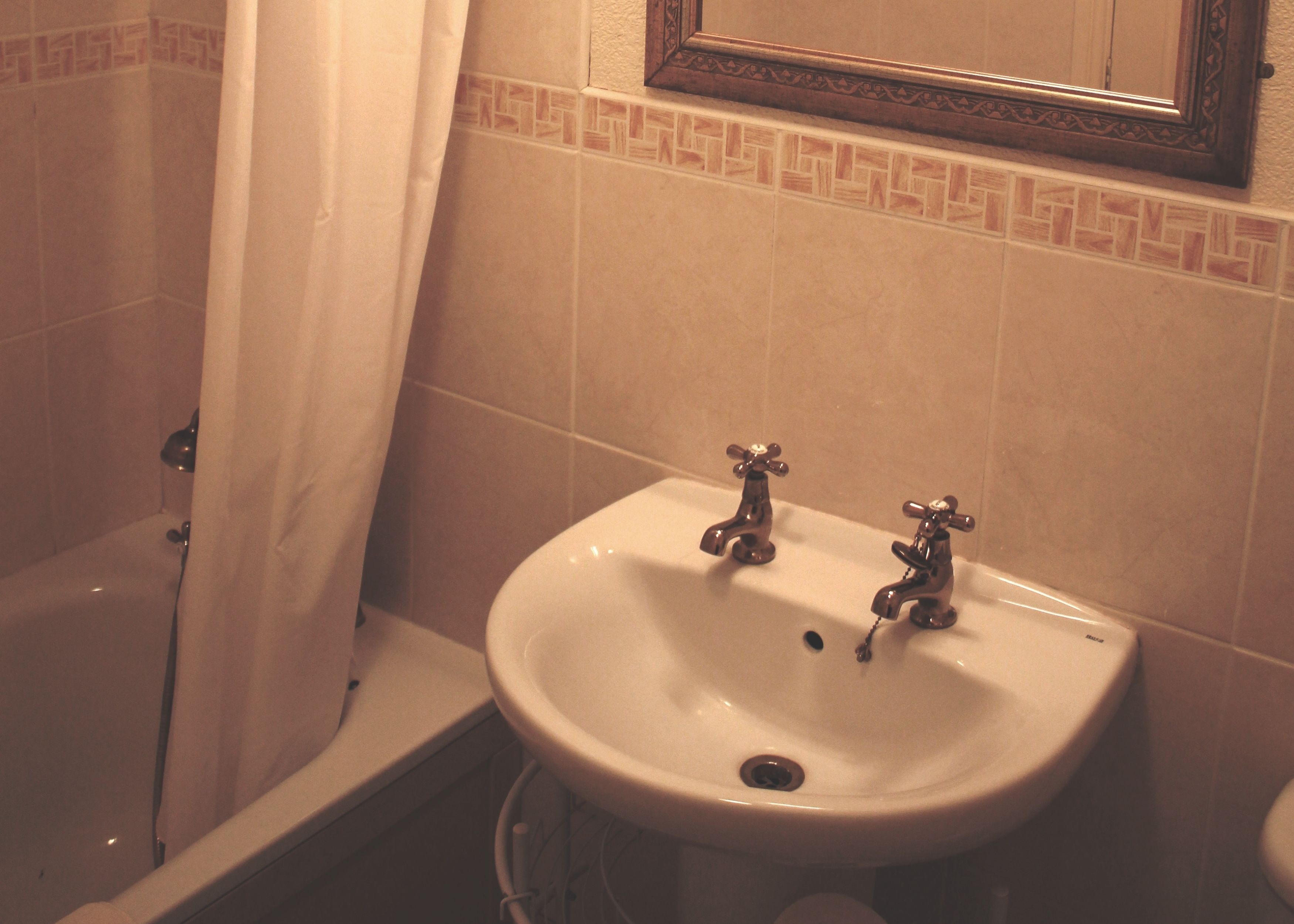 A bathroom with a bathtub, a sink with two faucets, and a mirror above the sink.