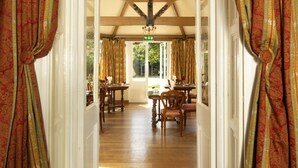 A room with a wooden ceiling, a dining table with chairs, and curtains with a pattern.