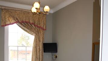A bedroom with a bed, a chair, a desk, a television, and a window with curtains.