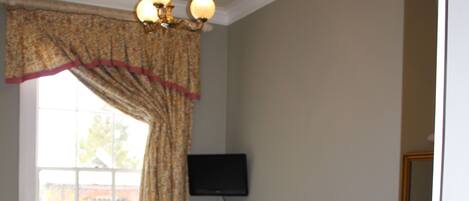 A bedroom with a bed, a chair, a desk, a television, and a window with curtains.