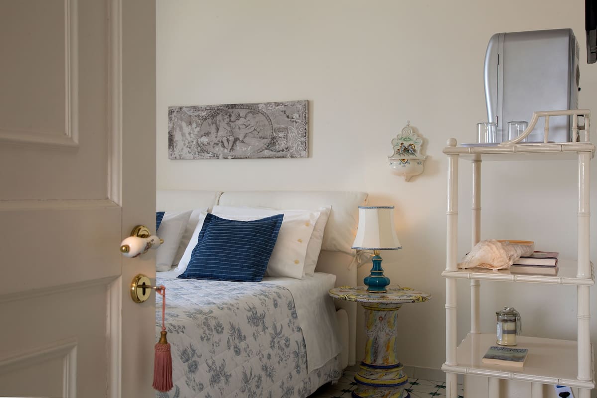Een slaapkamer met een bed, nachtkastje, lamp, plank en een deur.