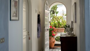 Ein Flur mit einer weißen Tür, einem gerahmten Bild, einem Blumentopf mit roten Blüten und einer Vase auf einem Tisch.