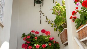 Ein rundbogiges Portal mit einem großen Terrakottatopf mit roten Blüten, einer wandmontierten Laterne und Kletterefeu.