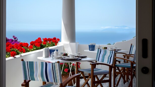 Eine Terrasse mit Esstisch, Stühlen mit gestreiften Kissen und Blick aufs Meer.