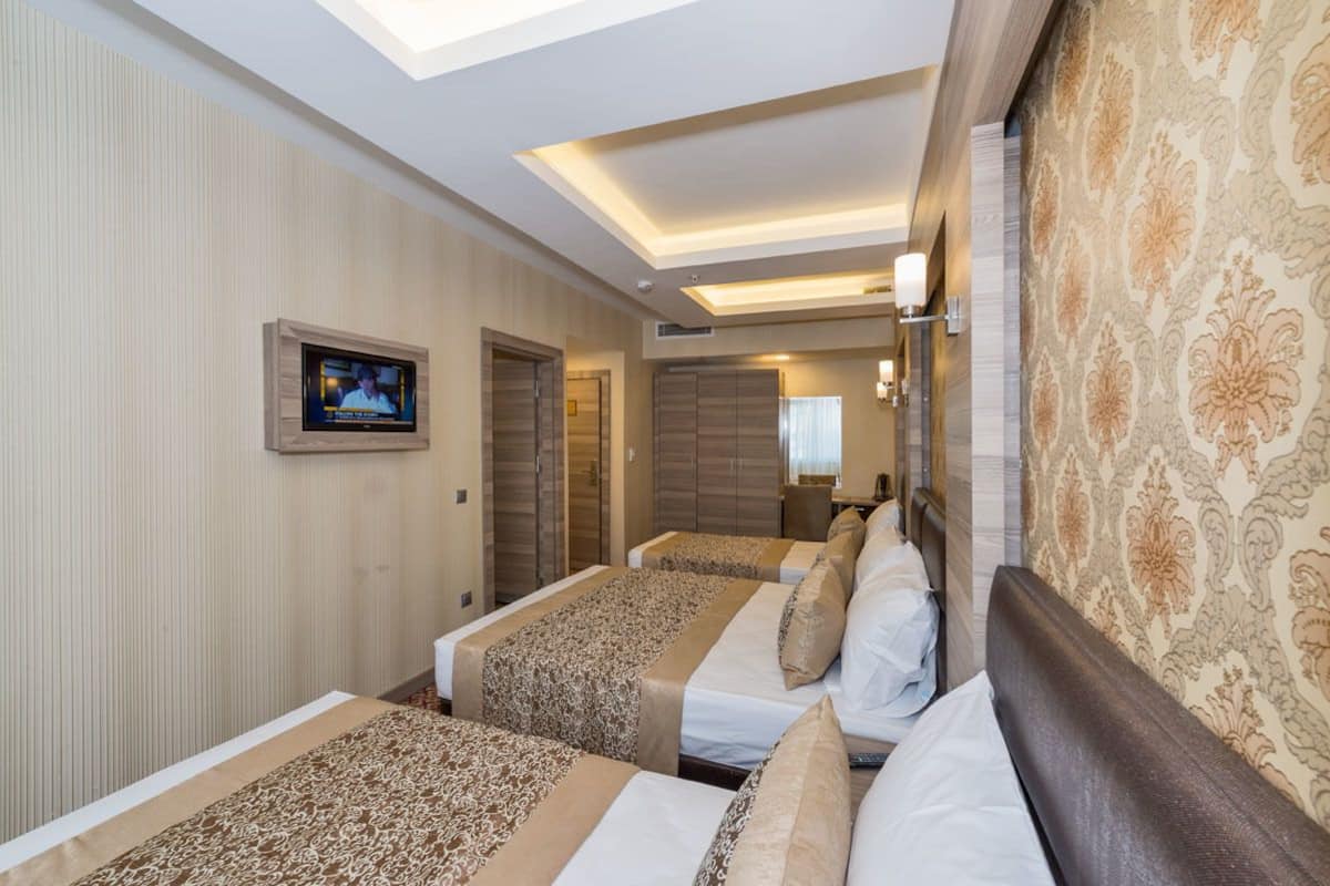 A hotel room with two beds, a TV, a ceiling light, and a patterned wall.