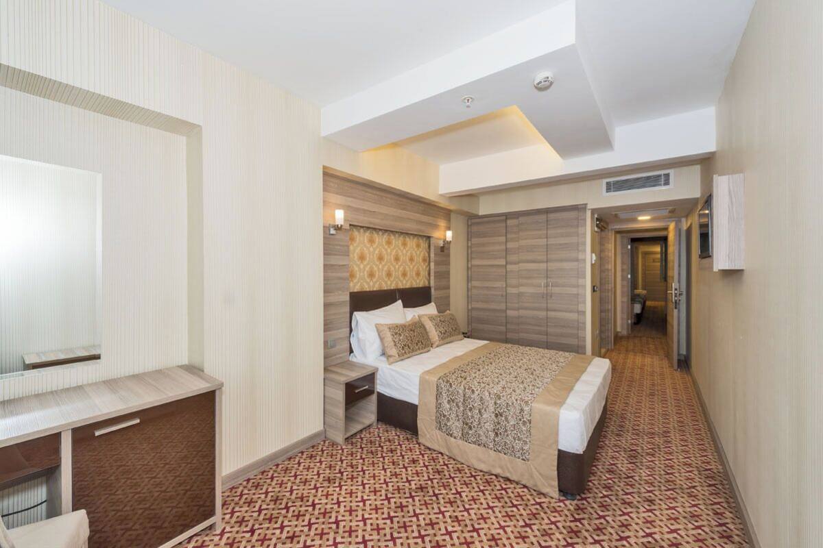 Ein Hotelzimmer mit Bett, Nachttisch, Kleiderschrank und Schreibtisch mit Stuhl.