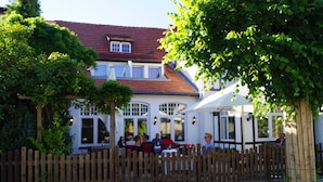 A traditional European-style building with a wooden fence, large windows, and outdoor seating for guests. - Landhaus Bode (Lübeck)