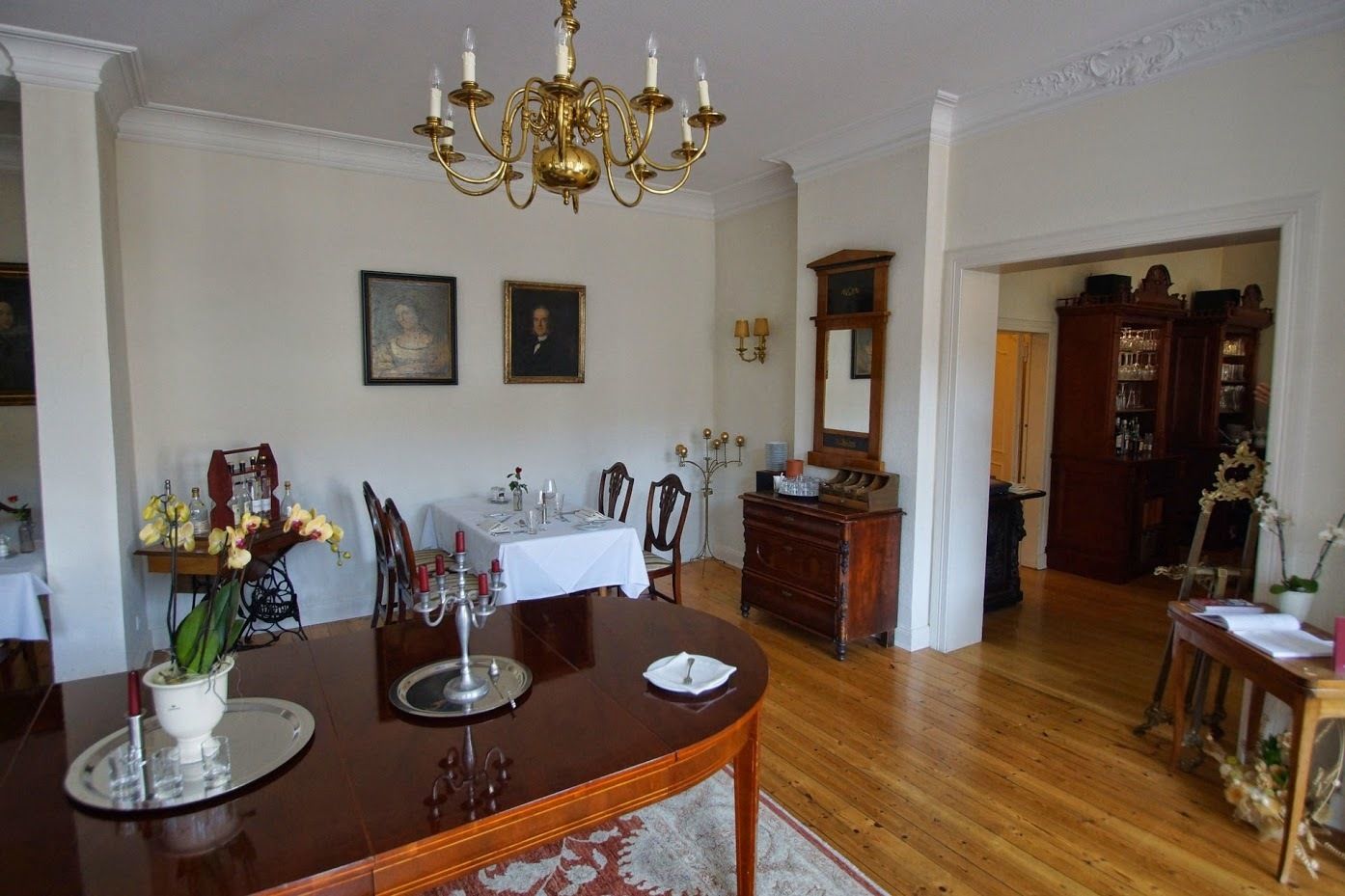 A dining room with a wooden table, chairs, a chandelier, and a mirror on the wall.
