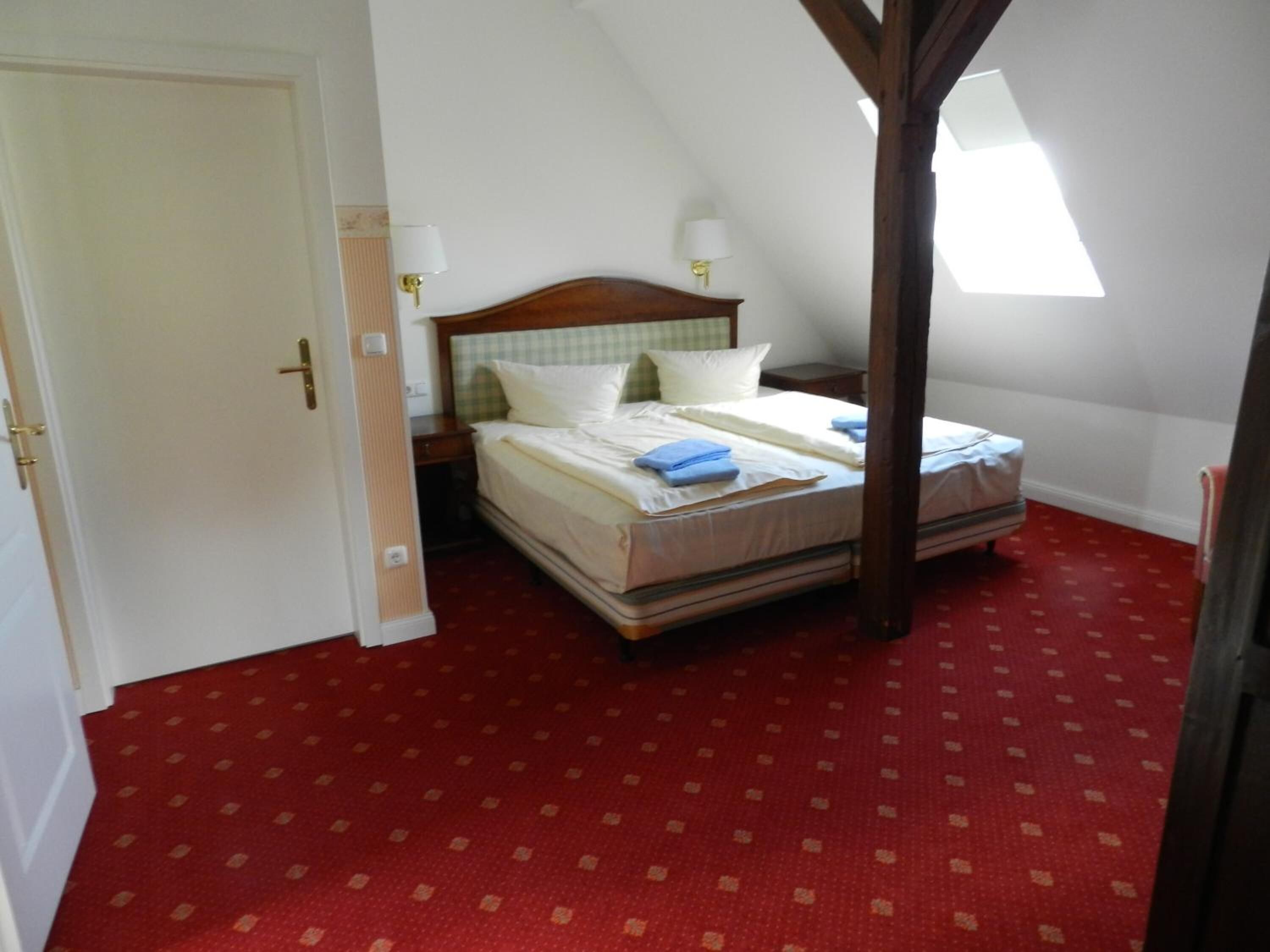 A bedroom with a double bed, two bedside tables, a window, and a red carpeted floor.