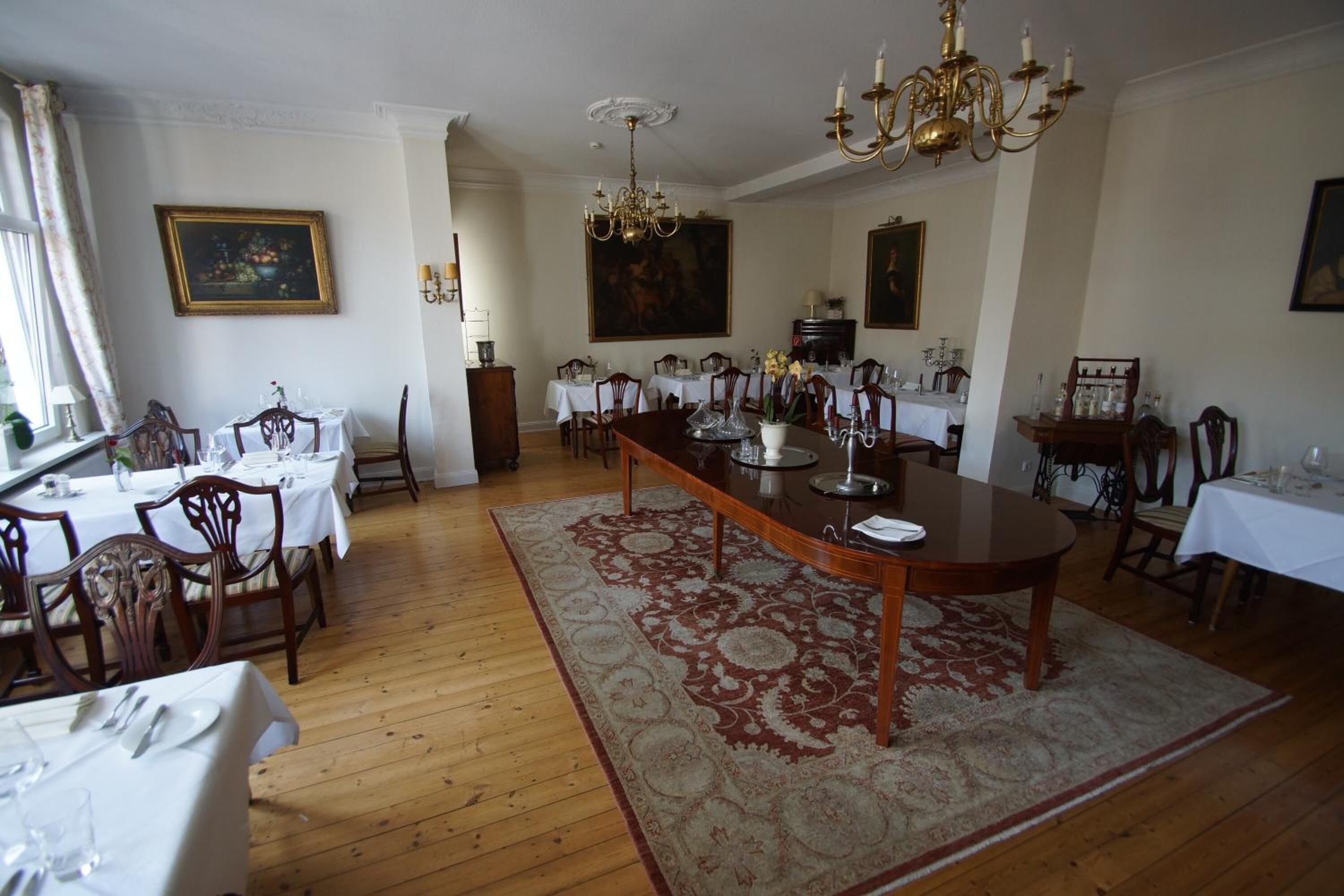Ein Esszimmer mit einem langen Holztisch, umgeben von Stühlen, gedeckt für eine Mahlzeit.