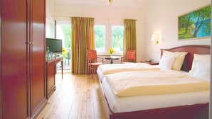 A hotel room with a large bed, a desk with a TV, a chandelier, and a painting on the wall. - Landhaus Bode (Lübeck)