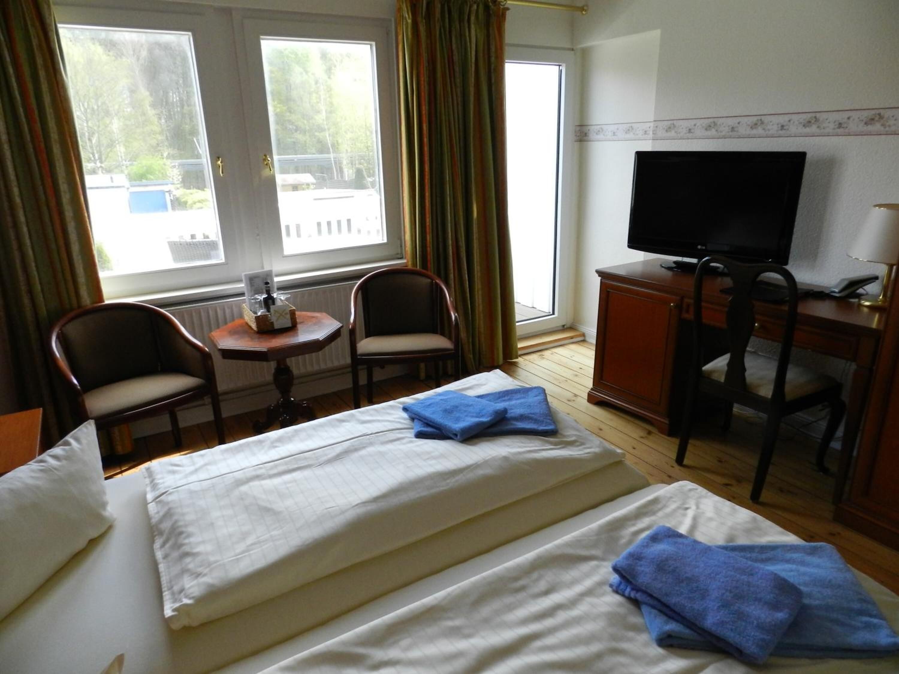 Une chambre d’hôtel comprenant un lit, deux chaises, un bureau avec une télévision et une fenêtre avec des rideaux.