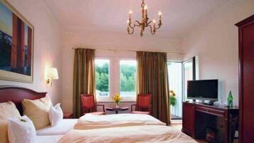 Ein Hotelzimmer mit einem großen Bett, einem Fernseher, einem Schreibtisch und einem Fenster mit Vorhängen.